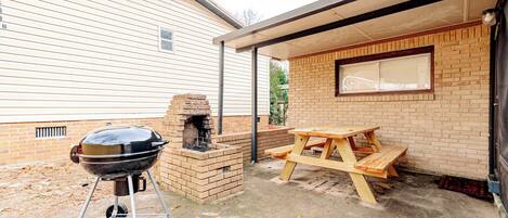 Een achtertuin met een bakstenen barbecue, een houten picknicktafel en een bakoven.