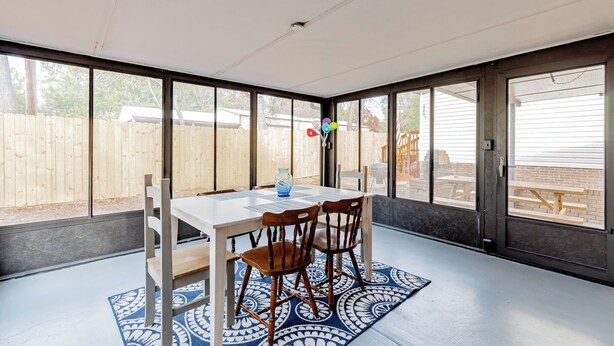 Un solárium con una mesa y sillas, ventanas amplias y vista a un jardín trasero.