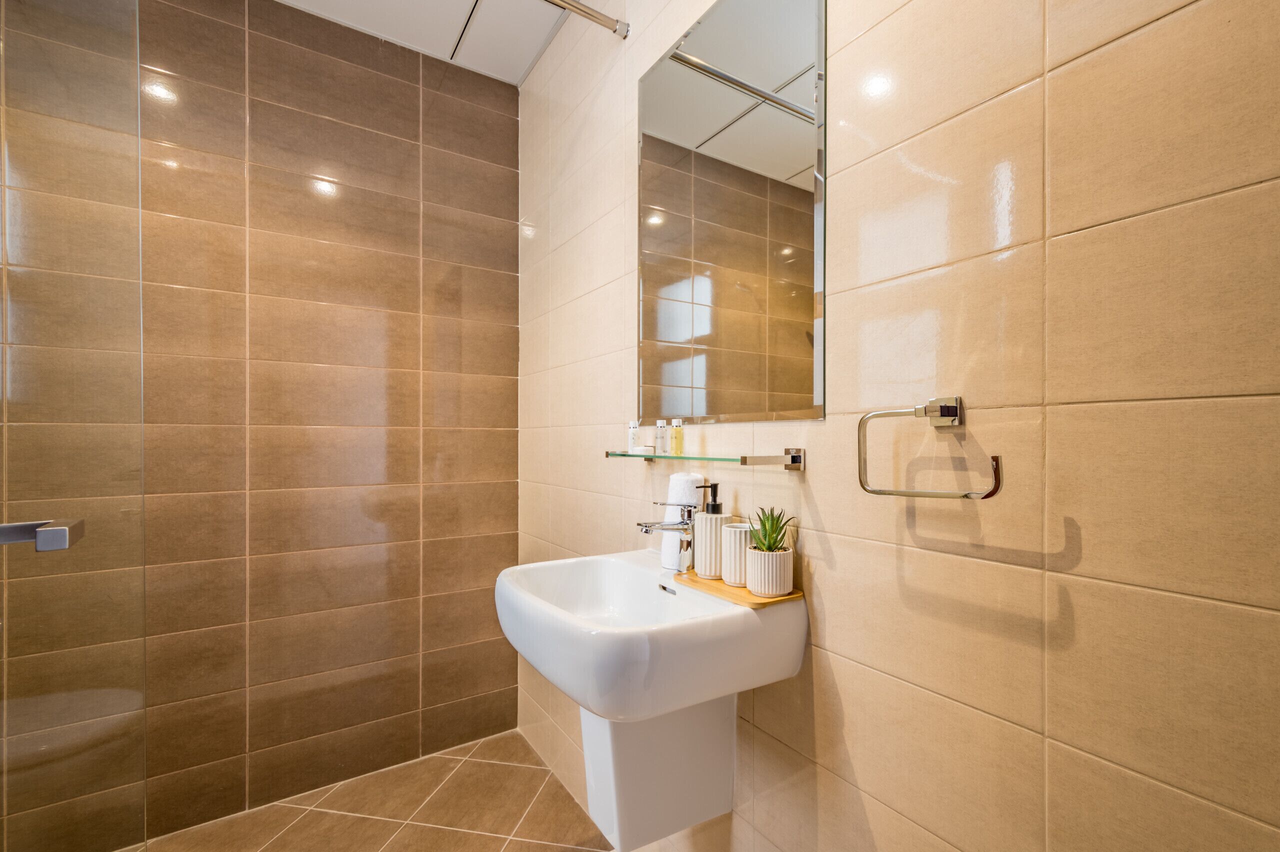 Een moderne badkamer met een wastafel op een zuil, een glazen plank met toiletartikelen en een grote spiegel.