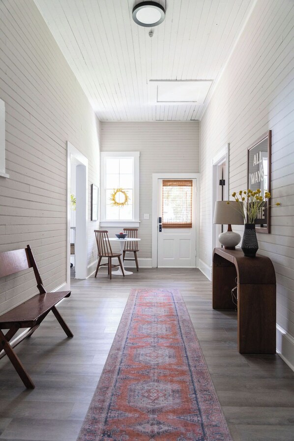A hallway with a wooden bench, a rug, a table with chairs, and a door with a wreath.