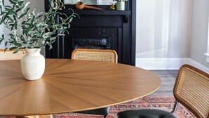Uma sala de jantar com uma mesa redonda de madeira, cadeiras de vime e uma lareira preta.