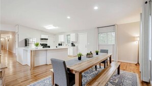 A modern kitchen with white cabinets, a central island, and a dining area with a wooden table and benches. - Columbia Duet Unit B (West Columbia)