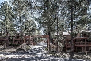 A gated entrance to Pinon Park condominiums with a stone pathway leading through a forested area. - Pinon Park C11 | Cozy, Fireplace, Great Location (Ruidoso)