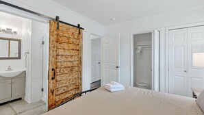 Une chambre avec un grand lit, une porte coulissante en bois, un lavabo blanc et un miroir.