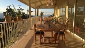 A covered outdoor patio with a wooden table and chairs, potted plants, and a view of the mountains.