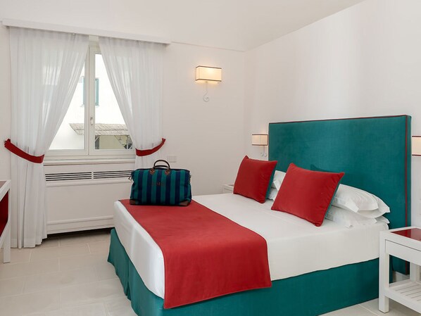 A hotel room with a bed, a nightstand, a window with curtains, and a wall-mounted lamp.