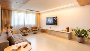Ein modernes Wohnzimmer mit einer Couch, zwei Sesseln, einem Couchtisch, einem an der Wand montierten Fernseher und einer Topfpflanze.