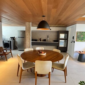 A modern kitchen with a central island, a dining area with a round table and chairs, and a large pendant light. - EDF. LUCIANE PEREIRA (Recife)