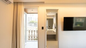 Ein Hotelzimmer mit Bett, Wand-Fernseher, Badezimmer mit Waschbecken und Spiegel sowie Blick ins Freie durch eine Tür.