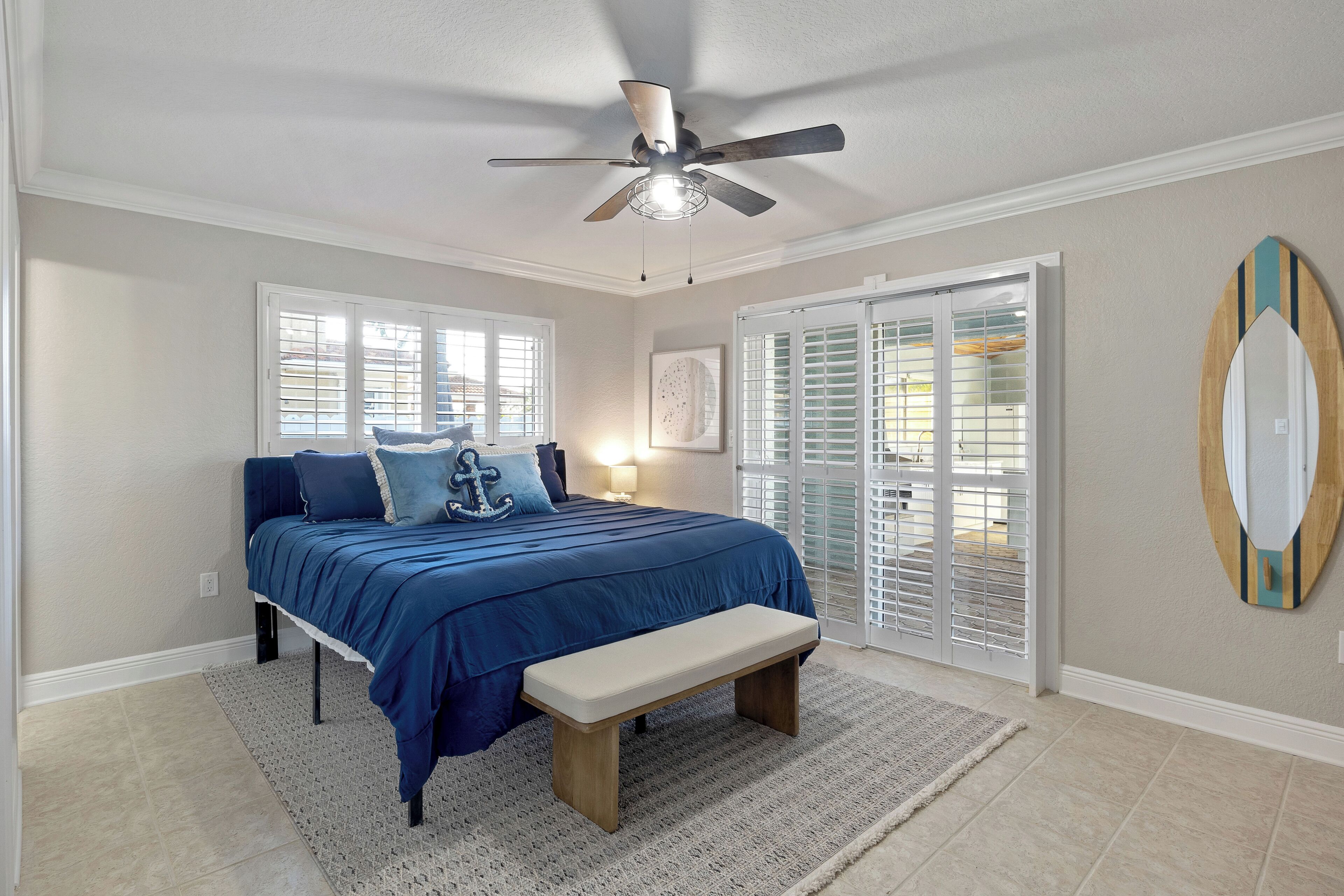 A bedroom with a bed, a ceiling fan, a bench, a window, and a door.