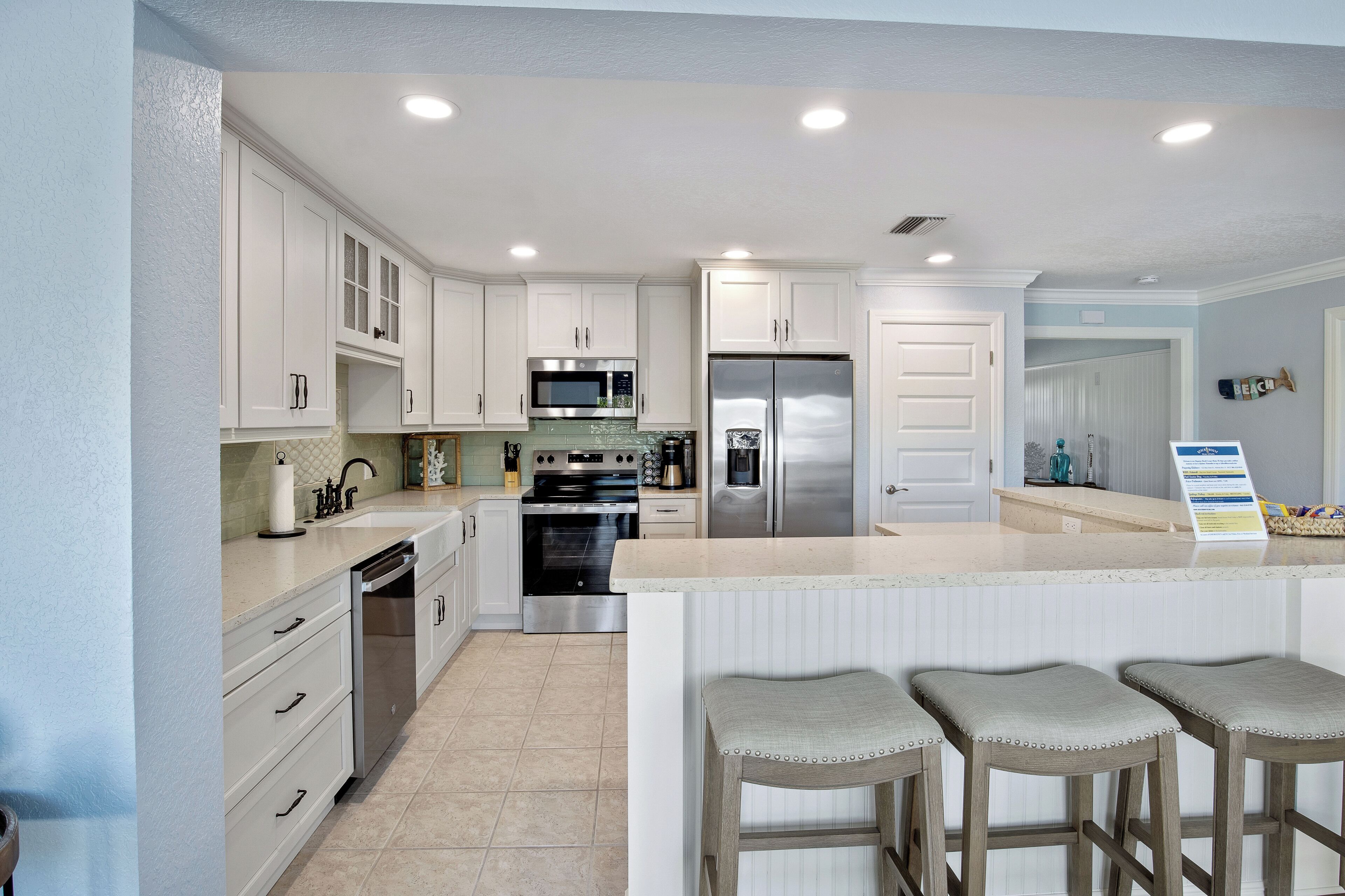 A modern kitchen with white cabinetry, stainless steel appliances, and a central island with bar stools.