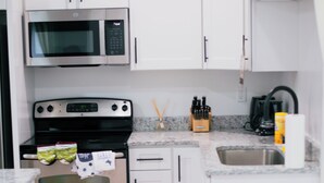 Una cocina con gabinetes blancos, un microondas de acero inoxidable, un horno y un lavabo.