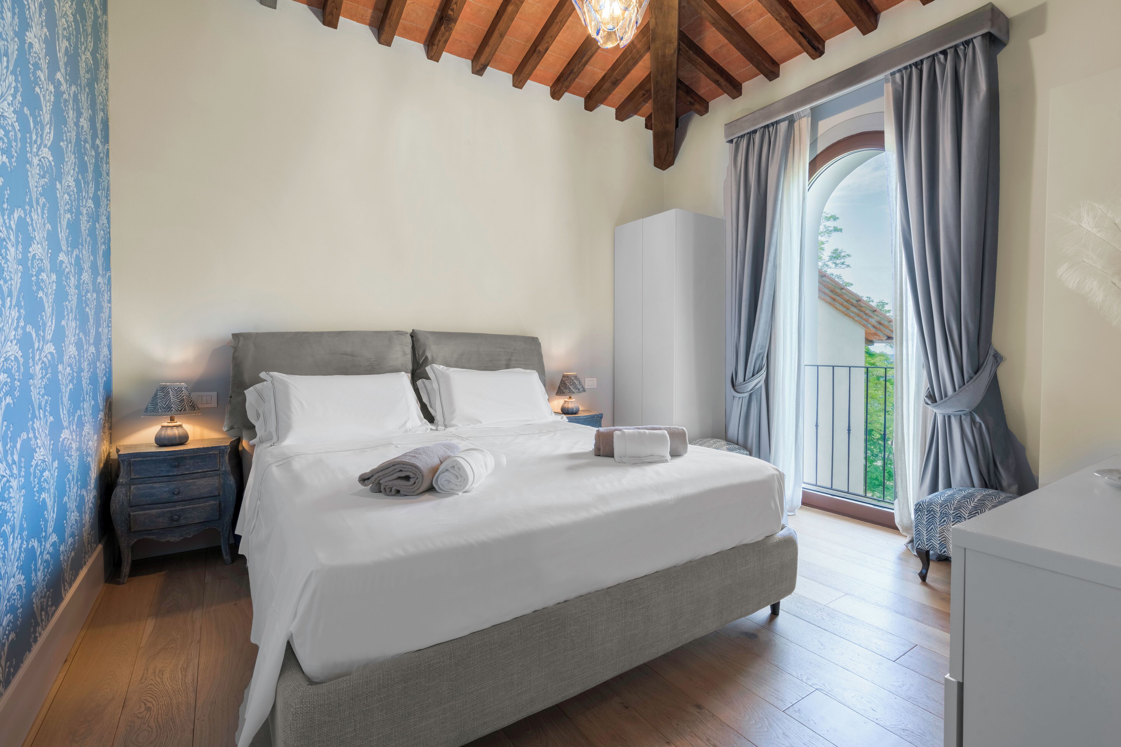 Une chambre à coucher comprenant un lit, des tables de chevet, une armoire et un balcon avec des rideaux.