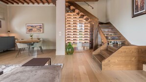 Un interior moderno con una escalera de madera, una zona de comedor con mesa y sillas, y una estantería para vinos.