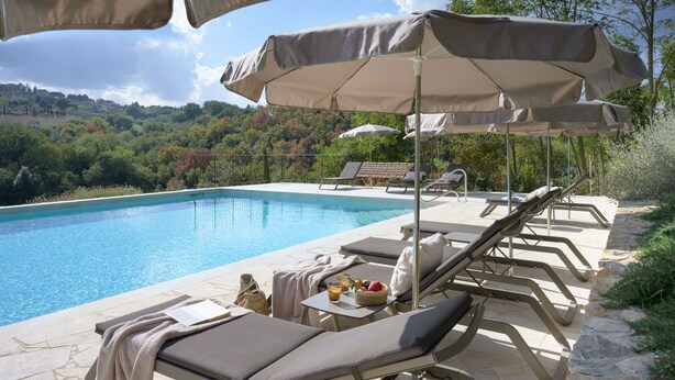 Zona junto a la piscina con sillones de descanso, sombrillas y vistas a un paisaje montañoso.