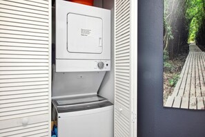 Et lille, hvidt vaskerum med vaskemaskine og tørretumbler indbygget. En seddel på tørretumbleren råder til at holde døren åben under tørring.