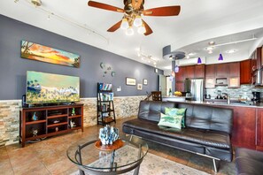 A living room with a TV, bookshelf, leather sofa, and a glass coffee table.