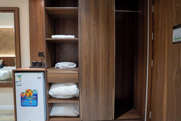 A hotel room with a wooden wardrobe, a minibar, and a bed with white bedding.
