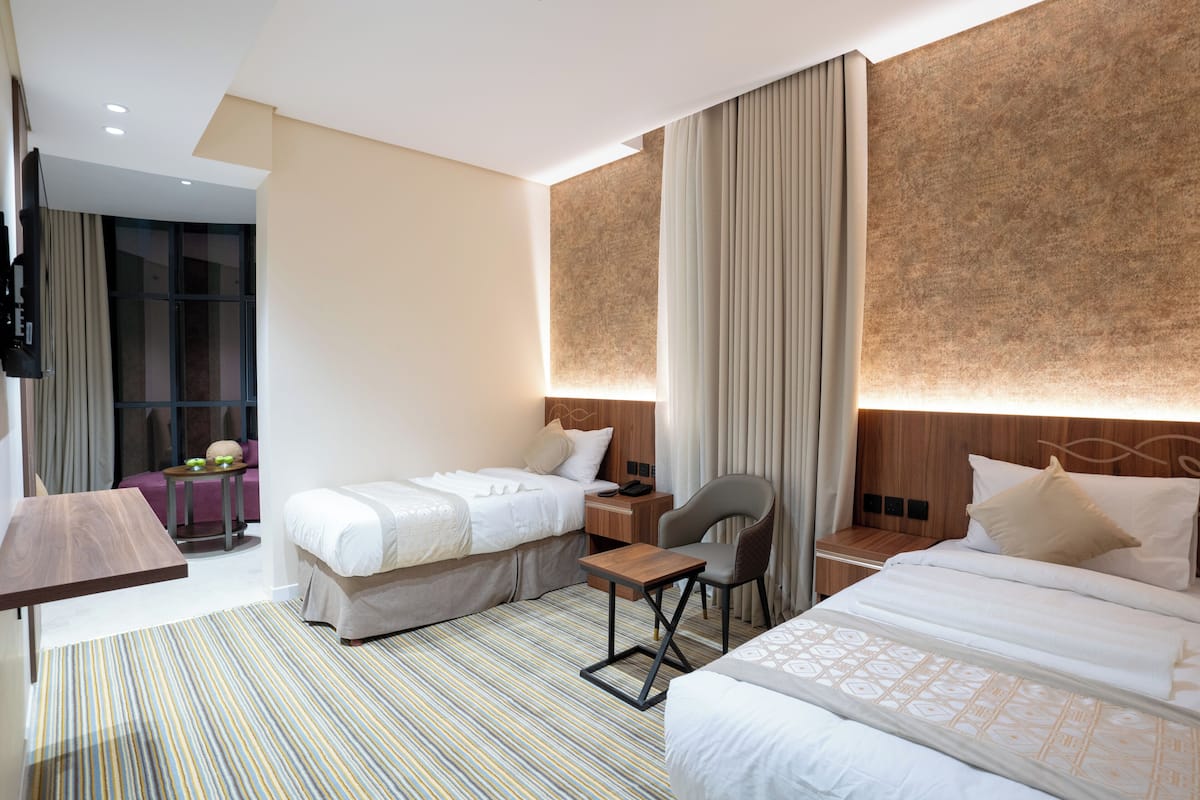 Habitación de hotel con dos camas, una mesita, una silla, un televisor y una ventana con cortinas.