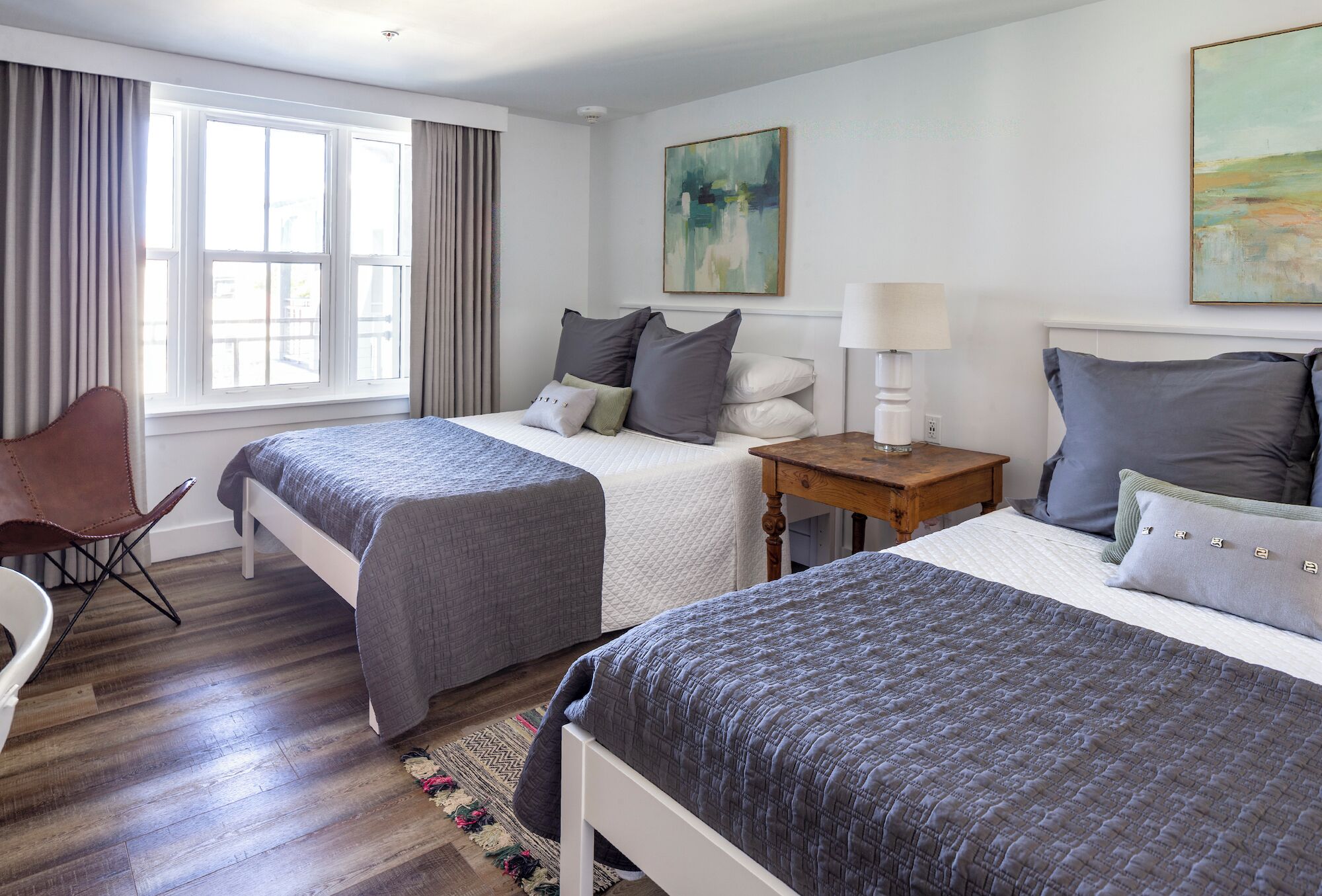 Habitación de hotel con dos camas, una silla, una mesita y una ventana con cortinas.