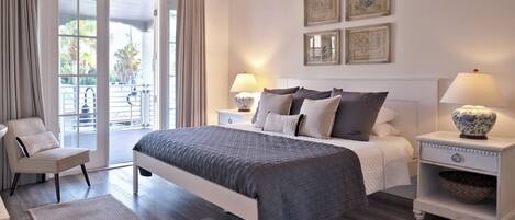A bedroom with a large bed, two bedside tables with lamps, a chair, and a view of the outdoors through a sliding glass door.