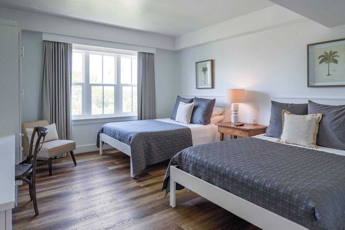 Een slaapkamer met twee bedden, een stoel, een bureau en een raam met gordijnen.