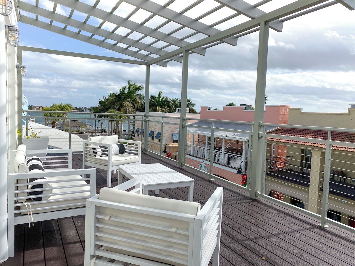 A covered outdoor seating area with white furniture, overlooking a cityscape with buildings and palm trees.
