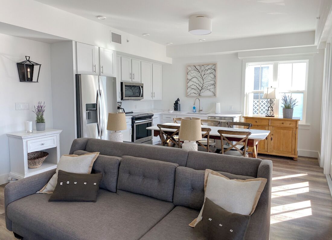 A modern kitchen with white cabinets, a stainless steel refrigerator, and a dining area with wooden tables and chairs.