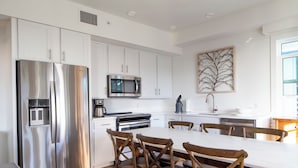Una cocina moderna con armarios blancos, electrodomésticos de acero inoxidable y una mesa de comedor de madera con sillas.