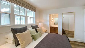 Un dormitorio con una cama grande, una mesita de noche, una lámpara, un espejo y vistas al baño a través de una puerta abierta.
