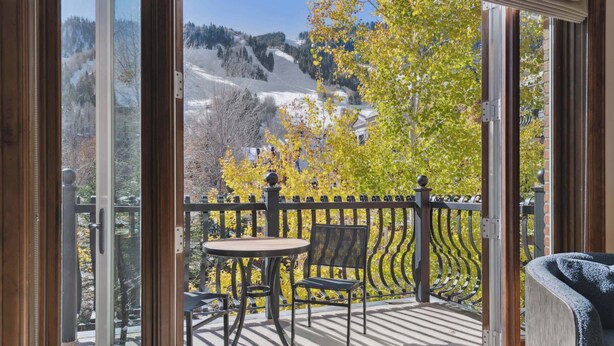A balcony with a table and chairs, a view of a mountainous landscape, and a wooden railing.
