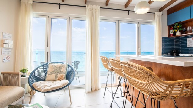Un soggiorno moderno con ampie finestre, angolo cottura e un balcone con vista mare.