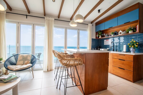 A modern kitchen with a central island, wooden cabinets, and a view of the sea through large windows. - Del Mare At Buye Beach Rooftop (Pedernales)