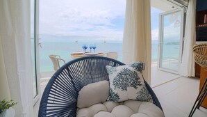 Un balcone con vista sul mare, una sedia in vimini, un tavolo con due bicchieri e un cuscino decorato con un motivo a foglia.