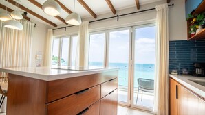 Una cucina moderna con una grande isola, mobili in legno e vista sull'oceano attraverso ampie porte scorrevoli.