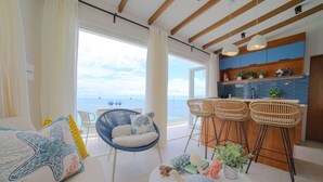 Un soggiorno moderno con un'ampia finestra, un divano con cuscini decorativi, una poltrona sospesa blu e un tavolino rotondo con un cuscino a forma di tartaruga.