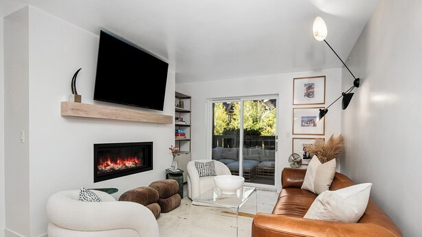 A modern living room with a fireplace, a flat-screen TV, comfortable seating, and a view through a glass door.