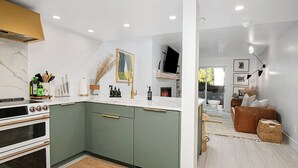 A modern kitchen with a built-in oven, a large island with a sink, and a dining area with a sofa and a coffee table.