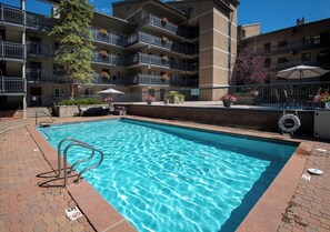A swimming pool with a metal ladder, surrounded by a brick walkway.