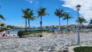 A stone-paved promenade with palm trees, a pool, and a view of resort buildings.