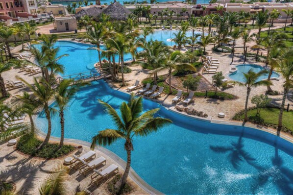 A resort with multiple swimming pools, palm trees, and lounge areas.