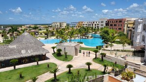 A resort with a central swimming pool, palm trees, and a thatched-roof building.