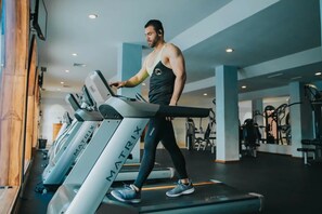 Een persoon die een loopband gebruikt in een sportschool, met diverse fitnessapparaten op de achtergrond.