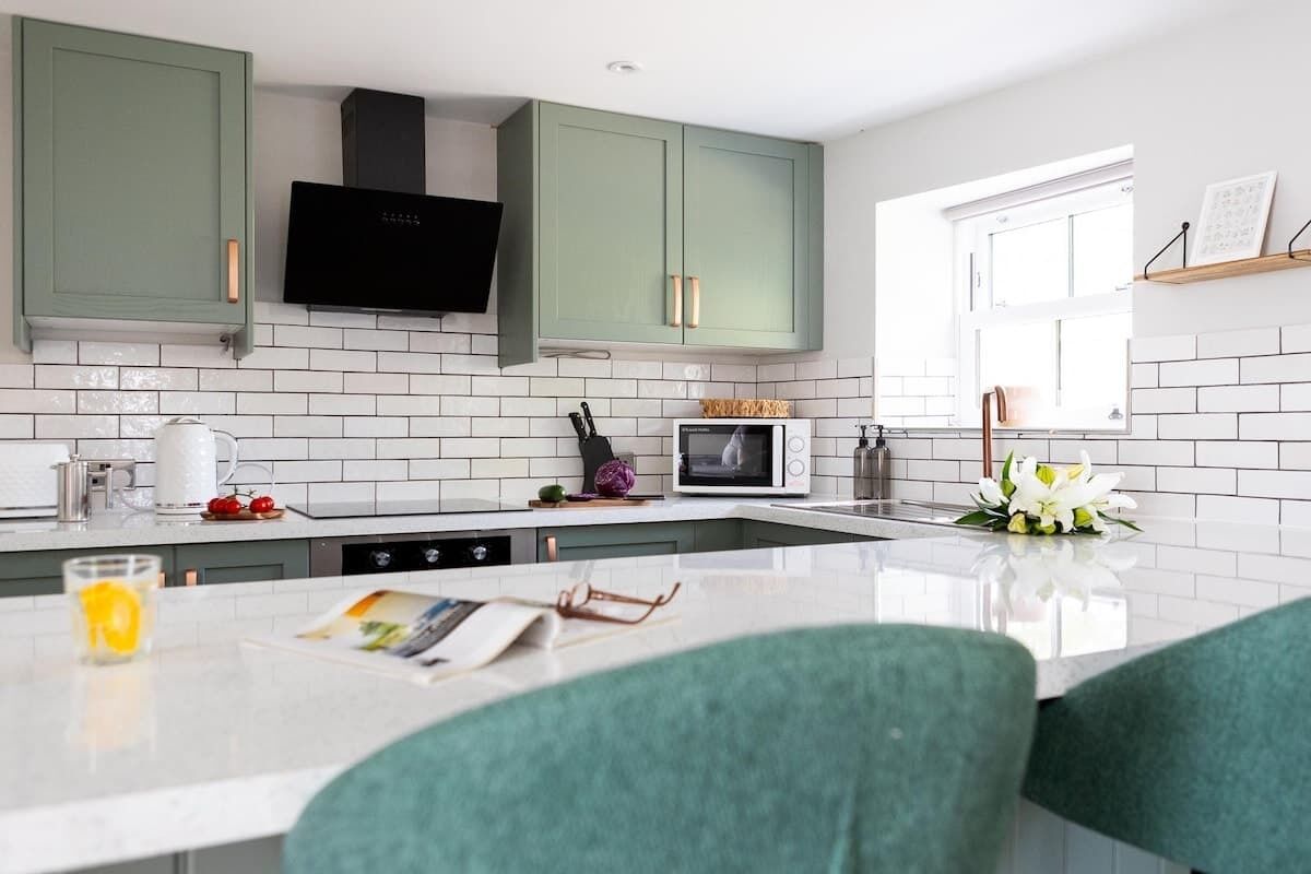 A modern kitchen with green cabinets, a white countertop, a built-in microwave, and a window providing natural light.