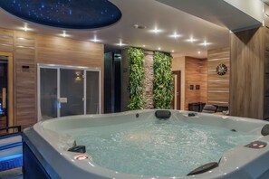 A modern spa room with a hot tub, wooden paneling, a stone wall with greenery, and a clock on the wall. - Hotel Panorama (Štrba)