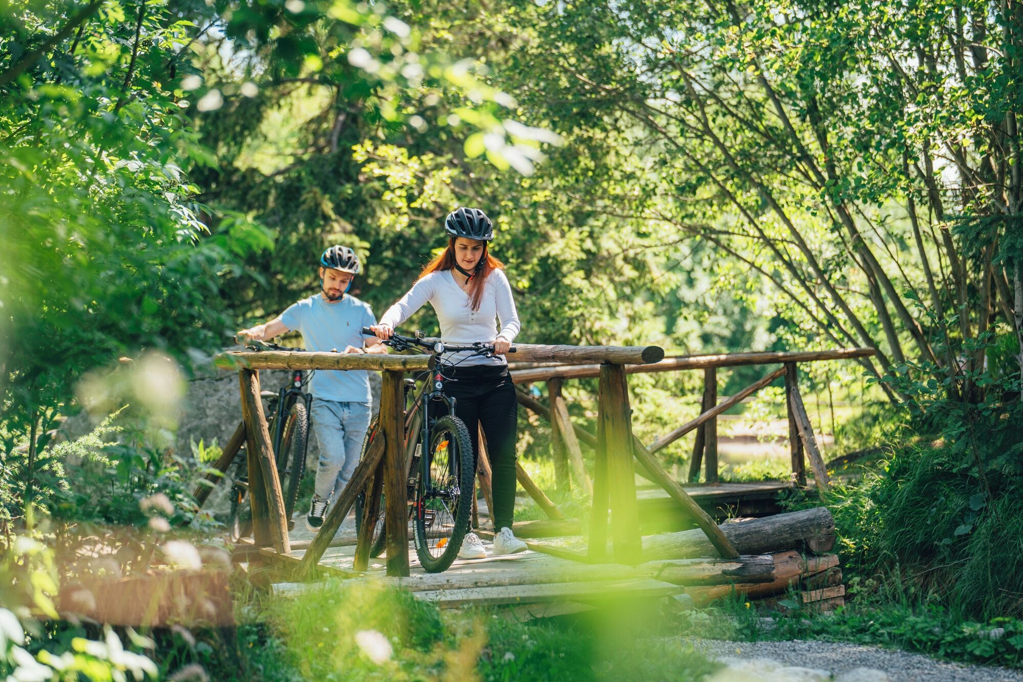 Two people on a wooden bridge in a forested area.