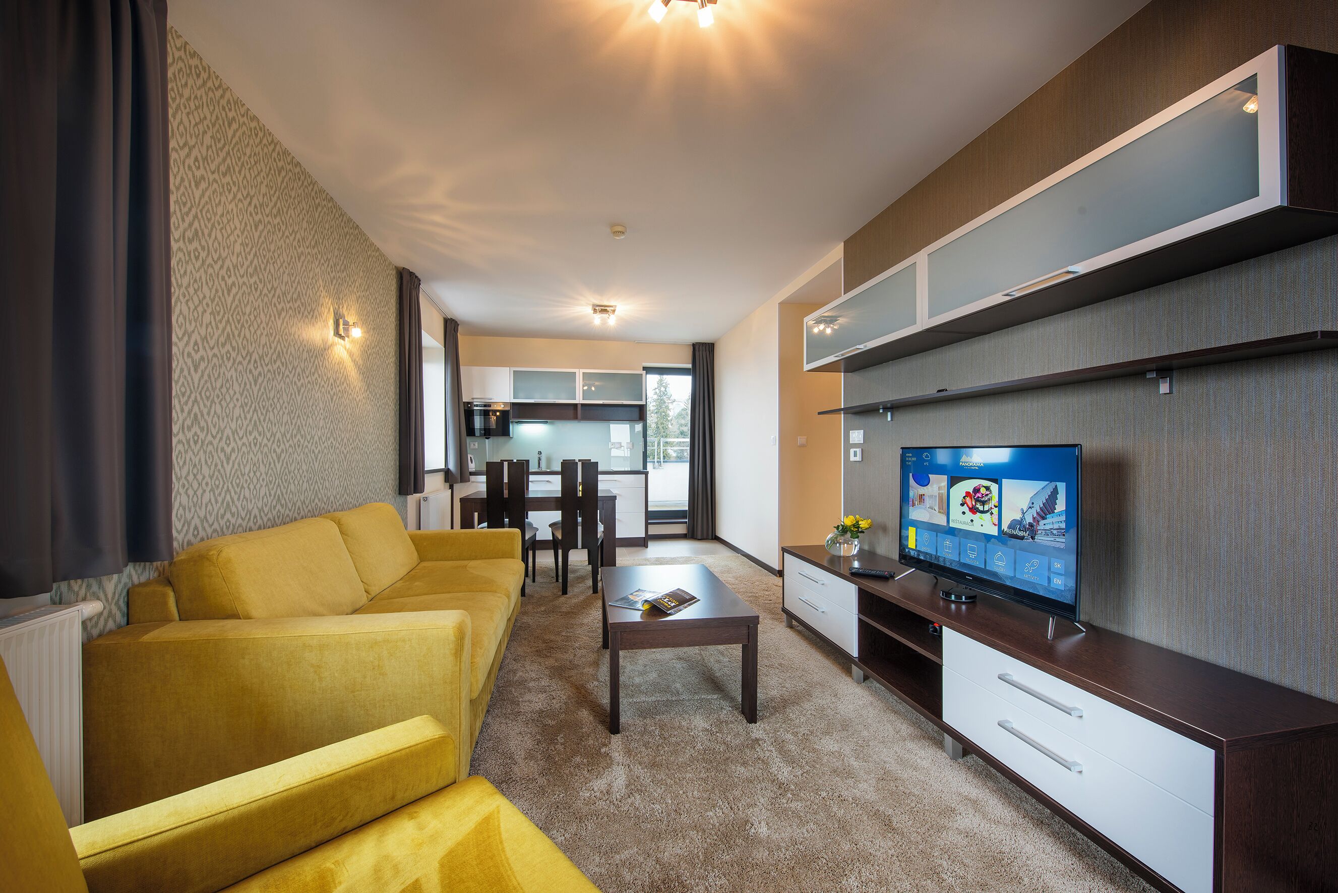 A modern living room with a sofa, coffee table, TV, and a dining area in the background.
