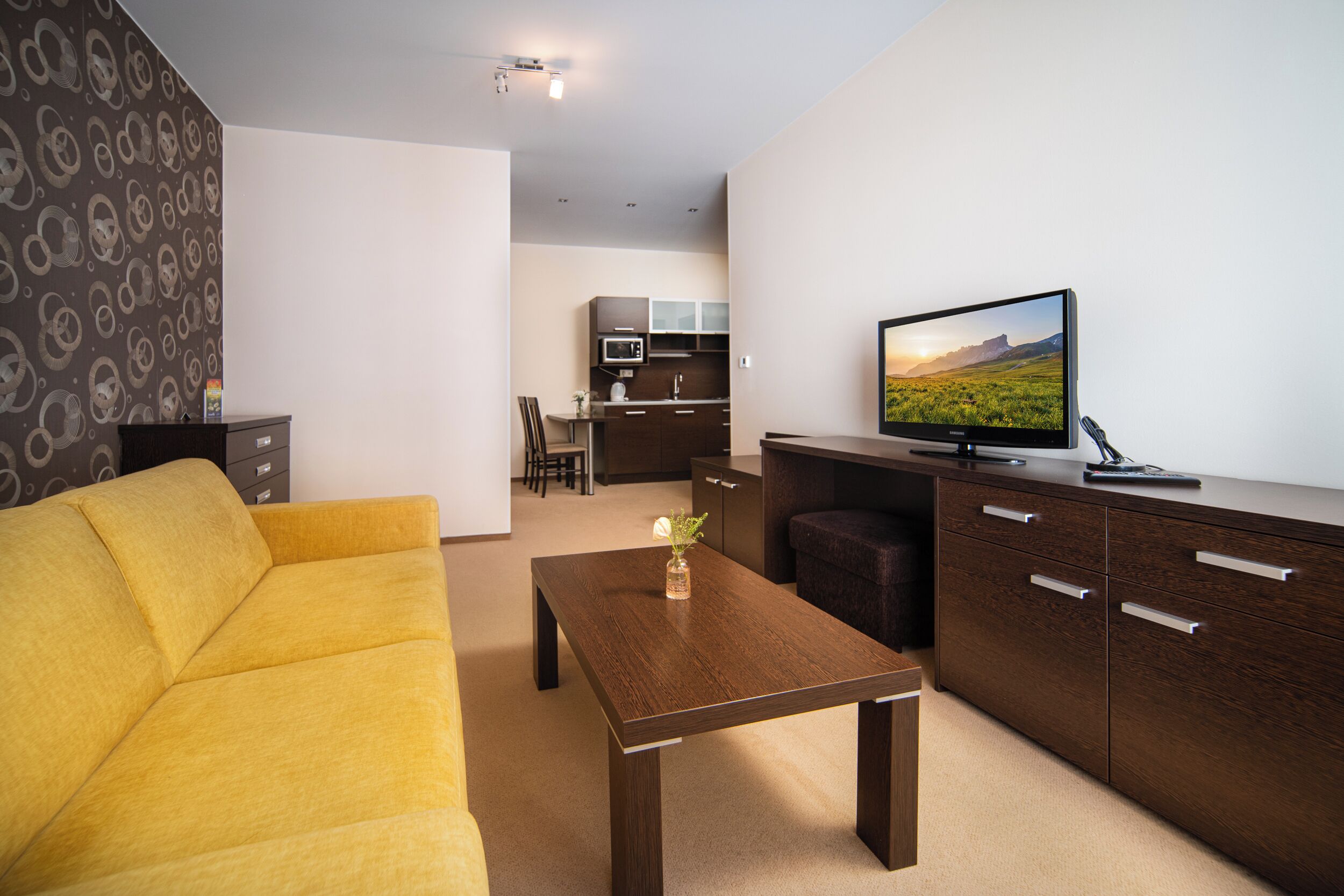 A modern living room with a sofa, a coffee table, a TV, and a kitchen area in the background.