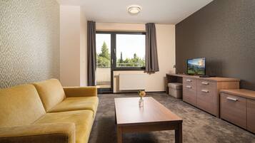 Una habitación de hotel moderna con sofá, una mesa de madera, televisión y vistas a zonas verdes.