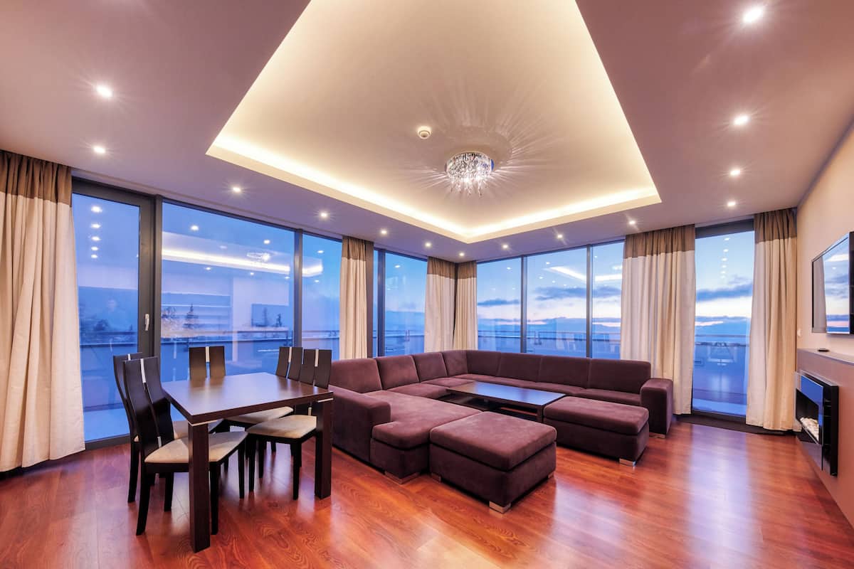 A modern living room with a sectional sofa, a dining table with chairs, and large windows offering a city view.